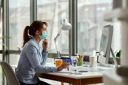 Young businesswoman wearing face mask while working on a computer in the office. 