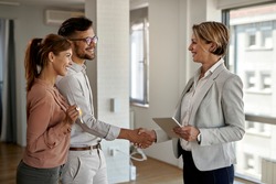 Happy real estate agent and young couple shaking hands after successful agreement. 