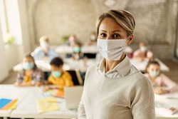 Female teacher wearing a face mask while teaching children at elementary school and looking at camera. 