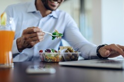 Close-up of businessman eating healthy food while using computer on lunch break in the office.