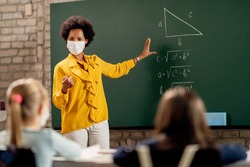 African American elementary school teacher holding mathematics class and wearing protective face mask due to coronavirus pandemic. 