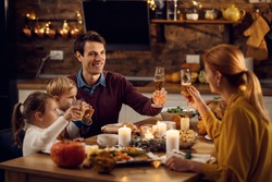 Happy family toasting while having Thanksgiving dinner at dining table. Focus is on father. 
