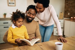 Happy African American family reading book together at home. 