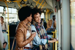 Happy black woman commuting with her female friend in a public transport. 