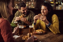 Happy woman having fun while talking to her friends and eating hamburger in a pub. 