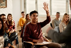 Smiling African American student raising his hand to ask a questing during a class at lecture hall. 