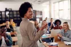 Happy African American professor receives applause from her students while lecturing them in the classroom.