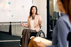 Happy CEO in wheelchair explaining inclusive business strategy to her coworkers during presentation in meeting room.