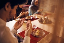 Close-up of Muslim man praying while eating with his family during Ramadan at home. 