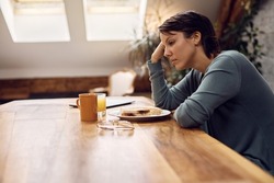 Thoughtful woman having no appetite while sitting at dining table at home. 