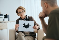 Mature mental health professional using Rorschach inkblot test to assess psychological condition of military man in her office. 