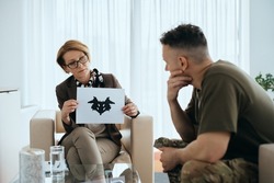Mature psychiatrist evaluating mental disorder of a soldier with inkblot test during counseling at her office.