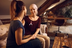 Smiling breast cancer ill woman communicating with female friend who is visiting her at home. 
