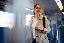Happy woman enjoying in train ride while drinking takeaway coffee. 
