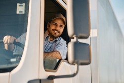 Happy professional truck driver driving his truck and looking at camera. Copy space.