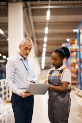 African American female worker and mature foreman using laptop while working at distribution warehouse. 