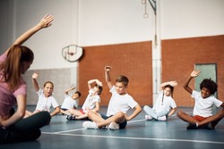 Group of kids doing stretching exercises with their PE teacher during a class at school gym. Copy space.