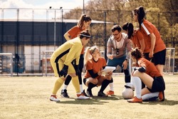 Young coach planning game strategy with female soccer team before the match. Copy space. 
