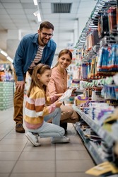 Happy parents and their daughter shopping school supplies in supermarket.