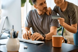 Close up of couple using credit card and computer while checking their online bank account at home.