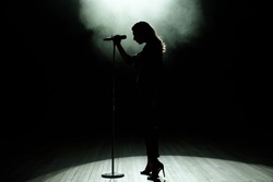 Black silhouette of female singer with white spotlights in the background.