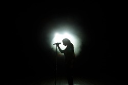 black silhouette of female singer with white spotlights in the background