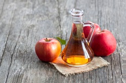 Glass bottle of organic apple cider vinegar with ripe fresh red apples on wooden background, selective focus, space for text