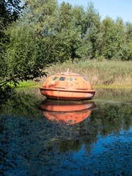 Vertical photo of an orange rescue pod or fully lockable lifeboat on the water