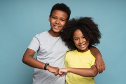 Awesome. Portrait of positive couple of brother and sister in casual style standing, hugging and bumping with fists with toothy smile, while looking at camera. Isolated, indoor, studio shot