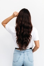 Woman from backside on white background. Female with curly hair. Rear view of brown-haired young lady with long hair, wearing white t-shirt over white background, isolated 