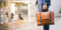 Closeup Of A Businessman wear the watch and Holding leather Briefcase Going To Work with the sunshine