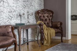 Close up of a vintage table and an armchair in a classical interior in italian style. Dark wooden furniture on a light walls, wooden floor. A perfect place to take rest. 