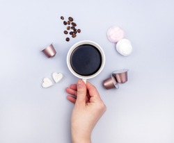 Top View Cup of Coffee Coffee Capsule Coffee Beans Sugar in Shape of Hearts Marshmallow Coffee Concept Background Blue Background Female Hand Holding Cup Flat Lay