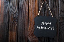 Happy Anniversary Sign Written In Chalk On Chalkboard On Rustic Vintage Wood Background. Top View Selective Focus.