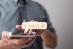 Close-up of a customer hand pressing on a smartphone screen with a gold five-star rating feedback symbol and a press level superb rank for providing the highest possible score to assess the service