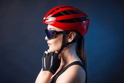 A young female cyclist wearing a safety helmet and glasses, dressed in a bib shorts poses against a black background in the studio.