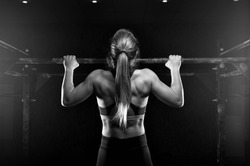 Young muscular woman doing pull up exercise on horizontal bar. Fit female practicing strength training. Fitness, sports concept.