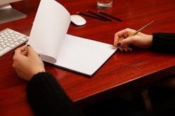 Woman signing a document or writing correspondence with a close up view of his hand with the pen and sheet of notepaper on a desk top. Folded sheet of paper