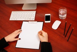 Woman signing a document or writing correspondence with a close up view of his hand with the pen and sheet of notepaper on a desk top. 