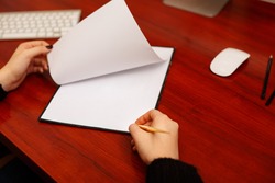 Woman signing a document or writing correspondence with a close up view of his hand with the pen and sheet of notepaper on a desk top.  Flipped documents