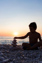 Little child playing with stones on the beach at sunset