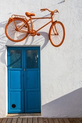 Orange bicycle hanging on a wall above a blue door