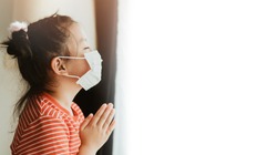 Little Chinese girl wearing mask for protect pm2.5 and coronavirus Covid-19.Stay at home praying to GOD.Online church worship in sunday.Little asian girl hand praying at home.Social distancing.