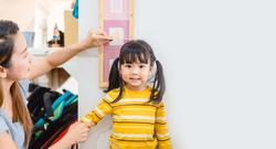 Mother Height measure her daughter near white wall at home.2.6 years old girl kid standing and looking at above using hand measuring her height.Growth hormones, child development, Calcium concept.