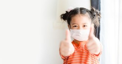 Coronavirus Covid-19 pm2.5.Online education.Little chinese girl wearing face mask show thumbs up for good and happy at home. Covid-19 coronavirus.Stay home.Social distancing.New normal behavior.