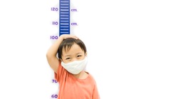 Height measure kid boy wearing mask.Kid measures the growth isolated white wall.3.6 years old boy kid standing using hand measuring his height.Growth hormones, child development, Calcium supplements.