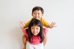 Cute Sibling sister and brother asian Korean Thai portrait kids.Asian children boy child siblings riding the back his sister on white wall at home.fun family.homeschool kid brother sister.hormones kid