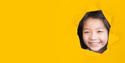 Asian Korean girl with funny face smile spy kid yellow paper break through banner.watching stubborn, kid child smile happy emotion.eye care in kid.crafty.happy child.School kid.stubborn tween girl.