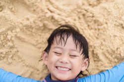5 years old asian boy lying and relax play sculpture white sand on the sea beach.Vacation and relax concept.Playful active kid on beach in summer vacation and child development.Asian kid boy smile.