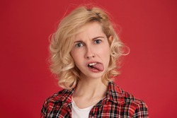 Attractive caucasian female shows her toung, feels disgust about new work week with bad people. Facial expression. Isolated over red background